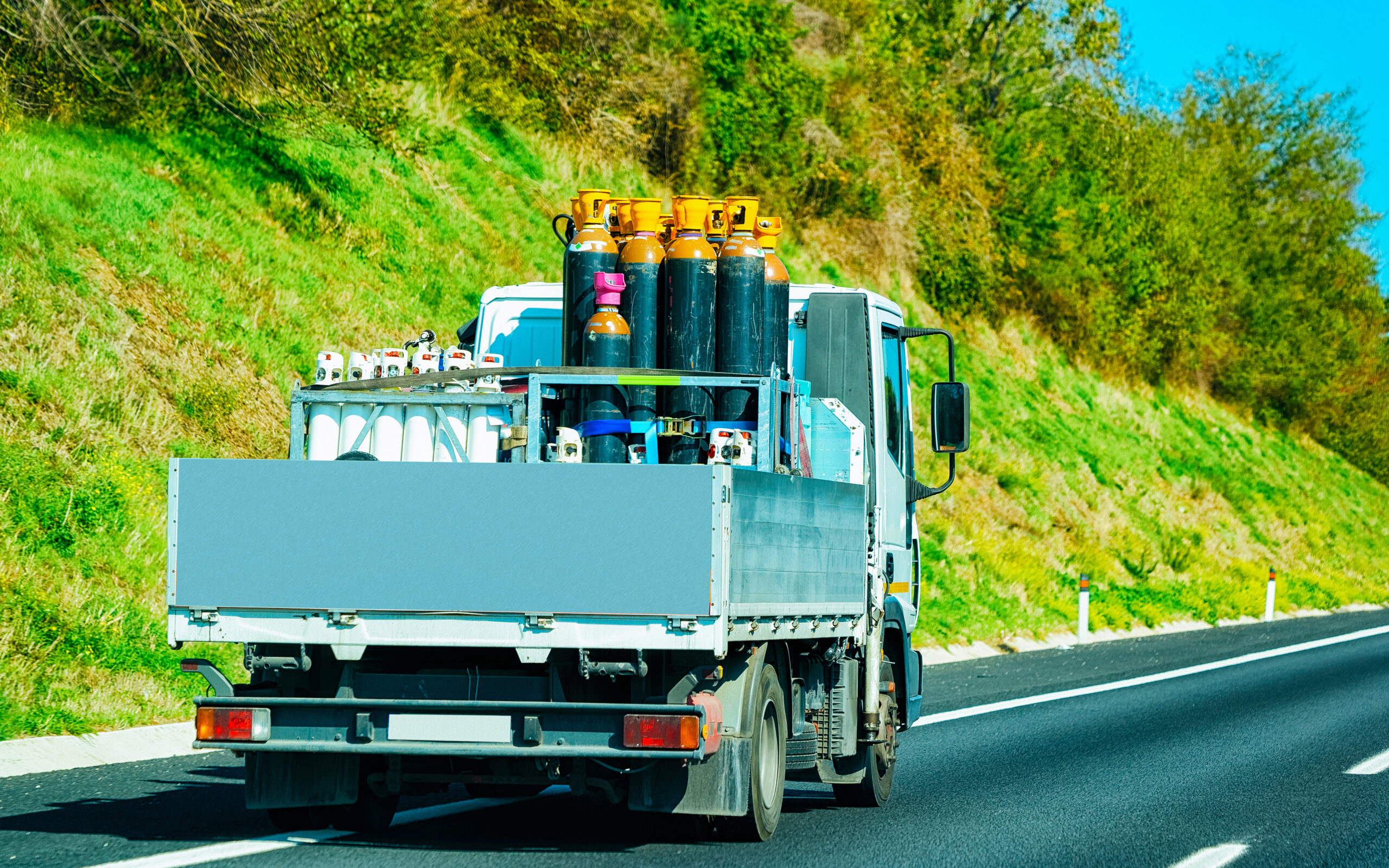 Flatbed delivery truck with gas cylinders driving on a highway.